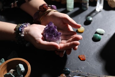 Photo of Woman with healing stones at black table, closeup