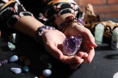 Photo of Woman with healing stones at black table, closeup