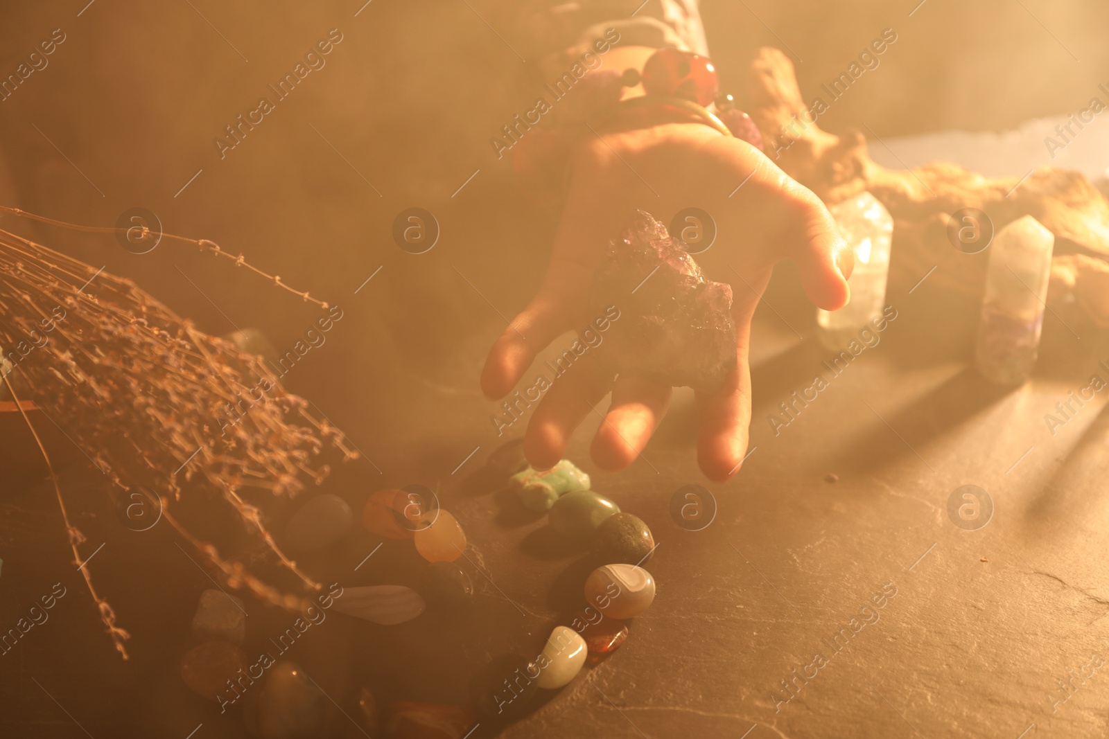 Photo of Woman doing ritual with healing stones at dark table, closeup