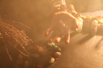 Photo of Woman doing ritual with healing stones at dark table, closeup