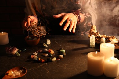Photo of Woman doing ritual with healing stones at dark table, closeup