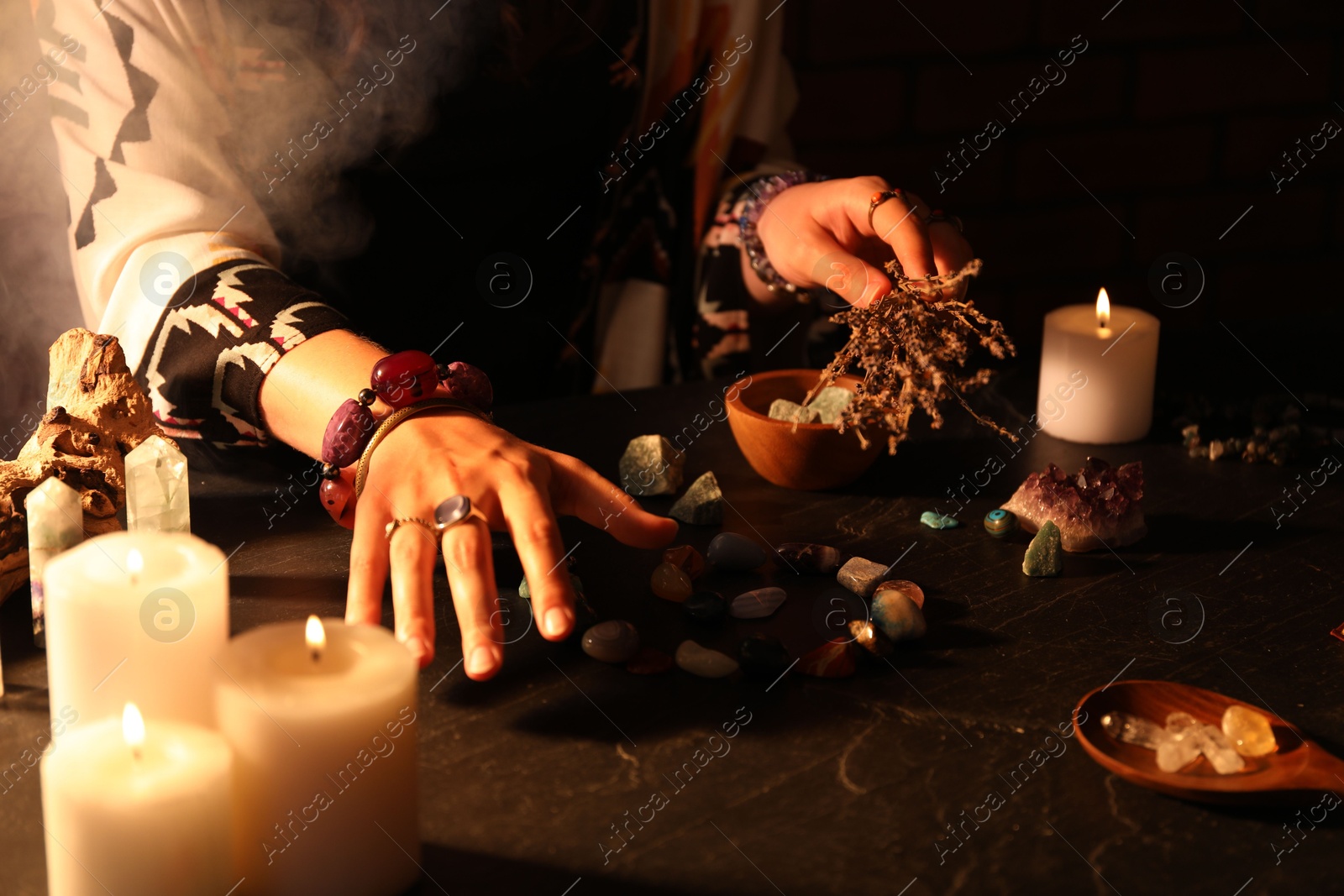 Photo of Woman doing ritual with healing stones at dark table, closeup