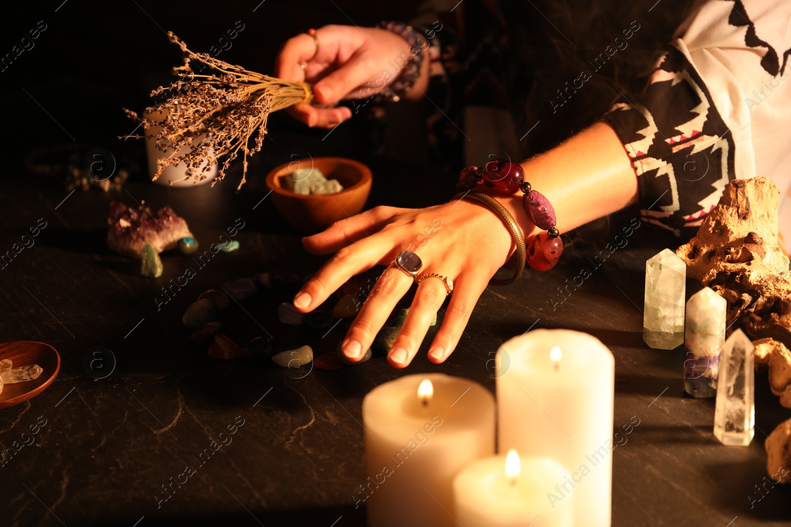 Photo of Woman doing ritual with healing stones at dark table, closeup
