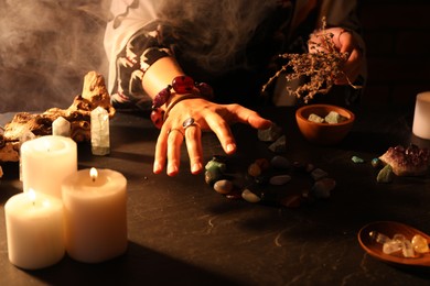 Photo of Woman doing ritual with healing stones at dark table, closeup