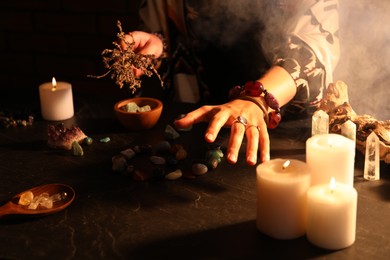 Photo of Woman doing ritual with healing stones at dark table, closeup