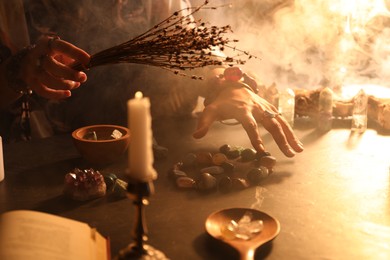 Photo of Woman doing ritual with healing stones at dark table, closeup