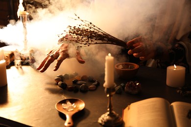 Photo of Woman doing ritual with healing stones at dark table, closeup