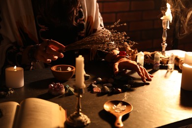 Photo of Woman doing ritual with healing stones at dark table, closeup