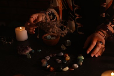 Photo of Woman doing ritual with healing stones at dark table, closeup