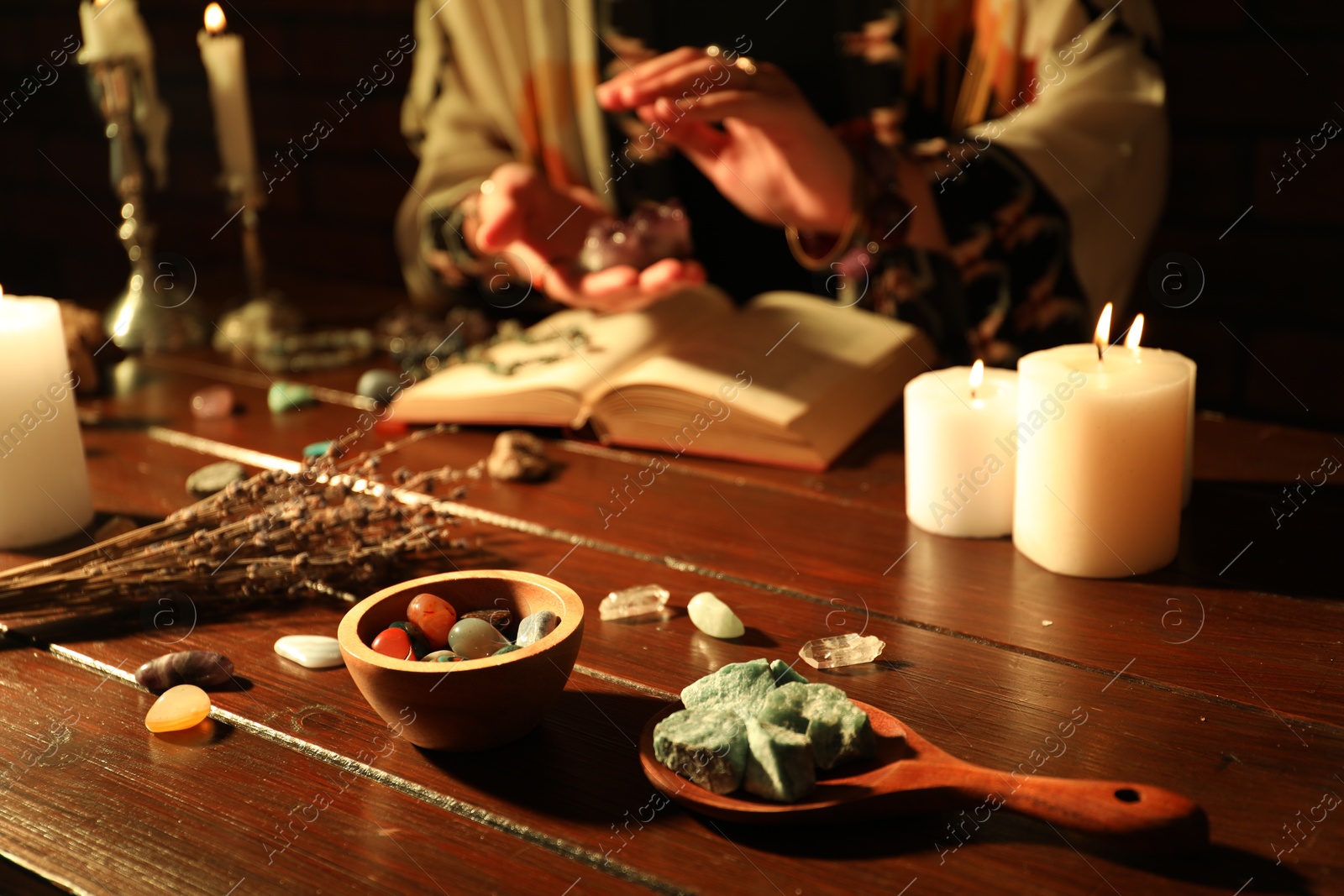 Woman doing ritual with healing stones at wooden table, closeup Photo of Woman doing ritual with healing stones at wooden table, closeup