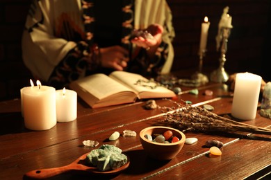 Photo of Woman doing ritual with healing stones at wooden table, closeup