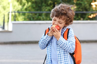 Photo of Cute little boy eating apple outdoors, space for text. School lunch