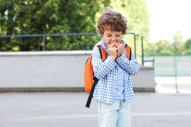 Photo of Cute little boy eating apple outdoors, space for text. School lunch