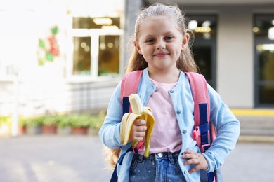 Photo of Cute little girl eating banana outdoors, space for text. School lunch