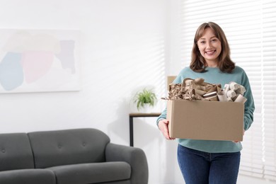 Photo of Recycling. Smiling woman holding cardboard box with different waste paper indoors. Space for text