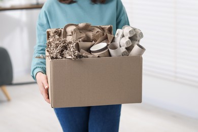 Photo of Recycling. Woman holding cardboard box with different waste paper indoors, closeup