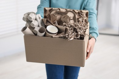 Photo of Recycling. Woman holding cardboard box with different waste paper indoors, closeup