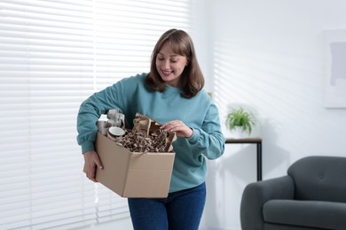 Photo of Recycling. Smiling woman holding cardboard box with different waste paper indoors