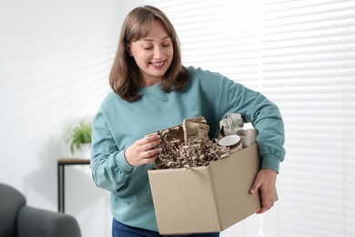 Photo of Recycling. Smiling woman holding cardboard box with different waste paper indoors
