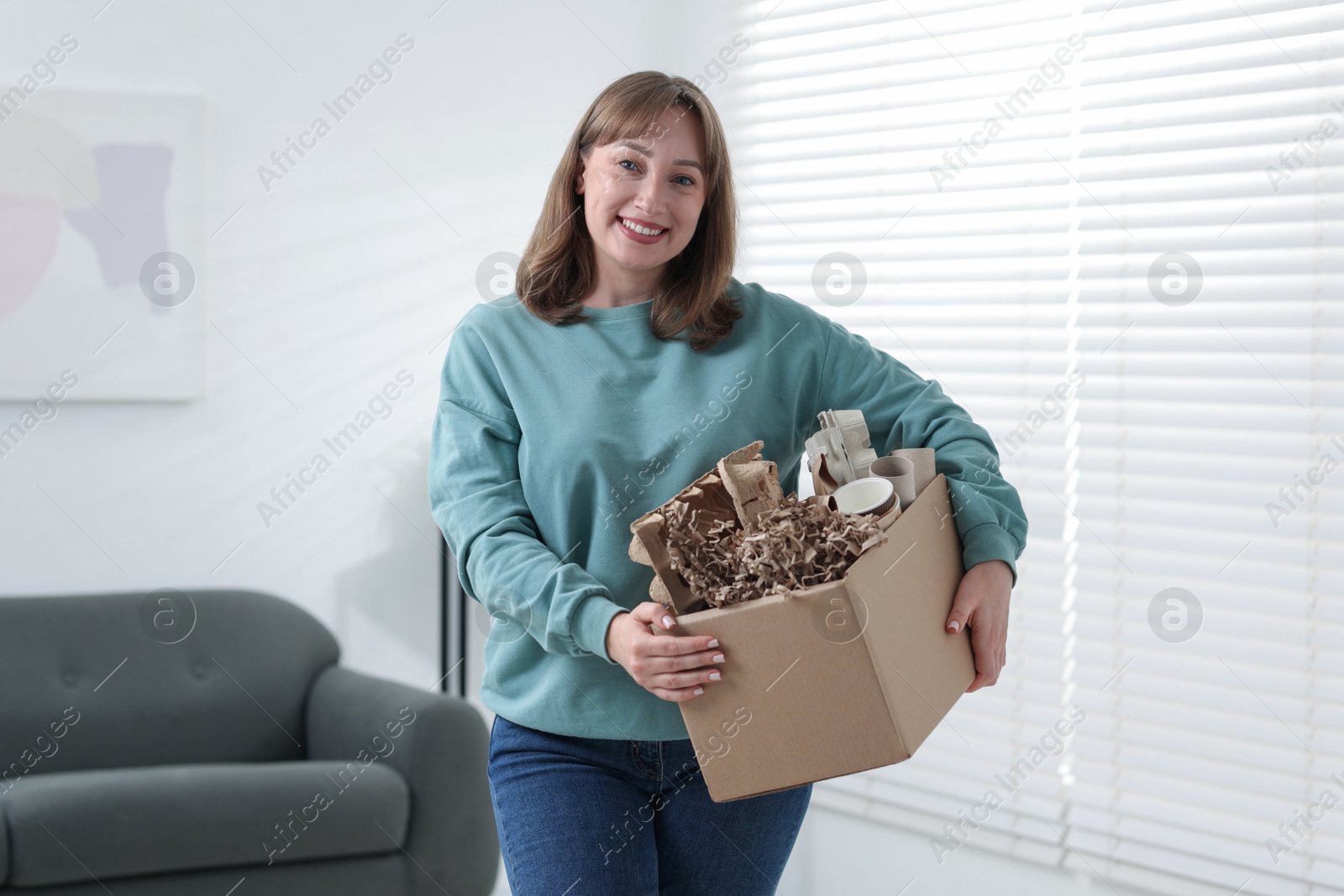 Photo of Recycling. Smiling woman holding cardboard box with different waste paper indoors
