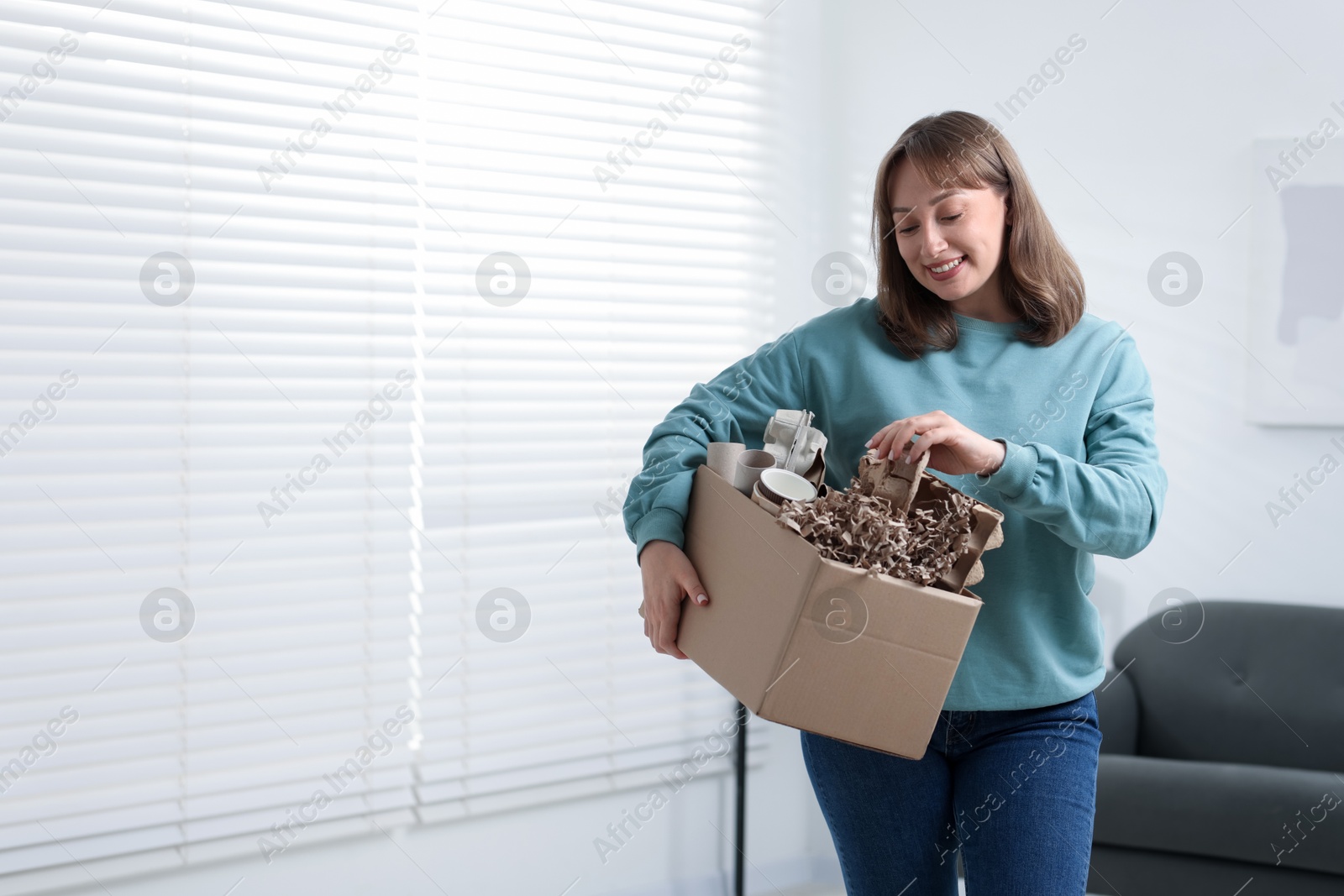 Photo of Recycling. Smiling woman holding cardboard box with different waste paper indoors. Space for text