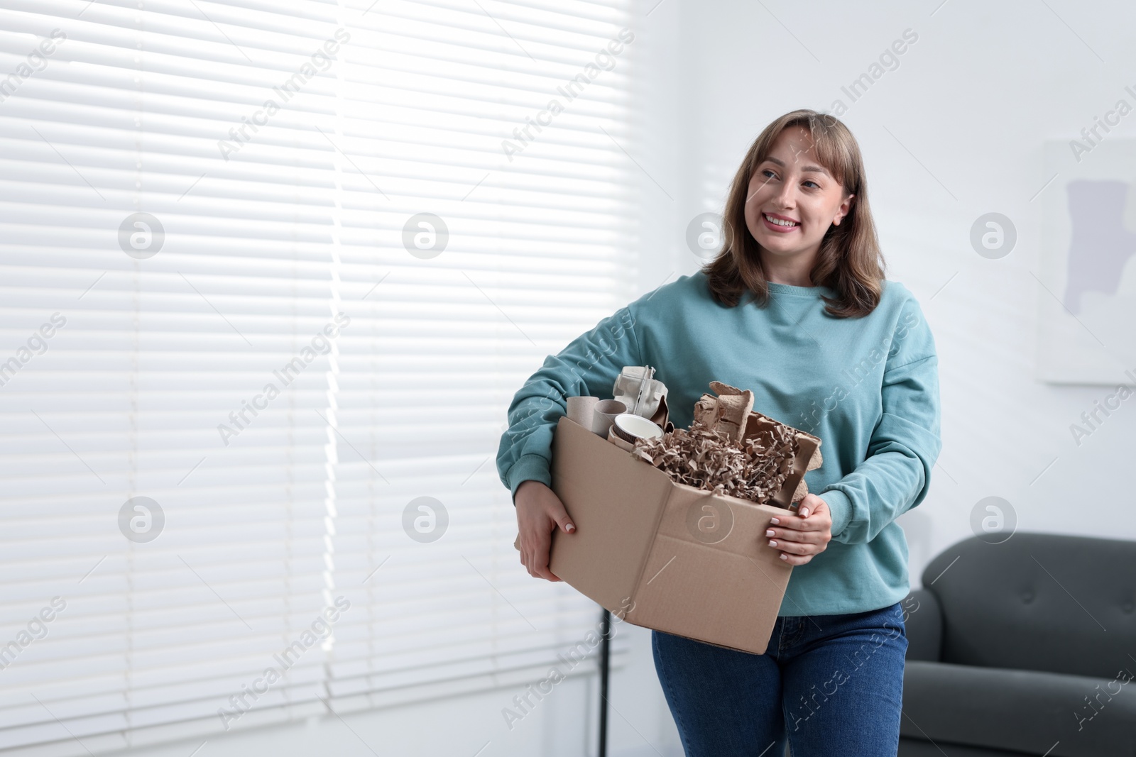 Recycling. Smiling woman holding cardboard box with different waste paper indoors. Space for text Photo of Recycling. Smiling woman holding cardboard box with different waste paper indoors. Space for text