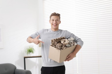 Photo of Recycling. Smiling man holding cardboard box with different waste paper indoors