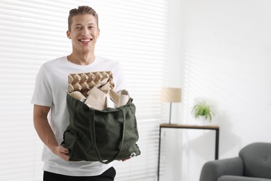 Photo of Recycling. Smiling man with bag full of different waste paper indoors. Space for text