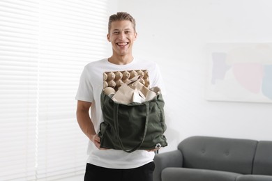 Photo of Recycling. Smiling man with bag full of different waste paper indoors