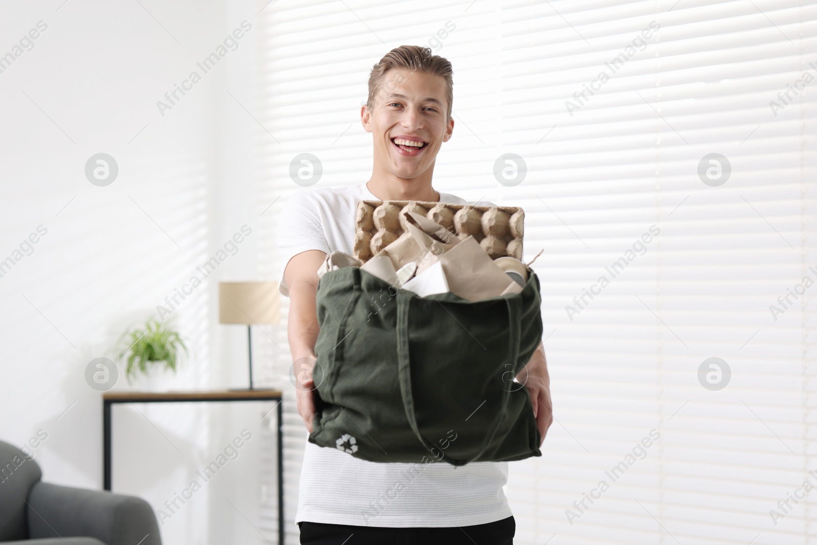 Photo of Recycling. Smiling man with bag full of different waste paper indoors