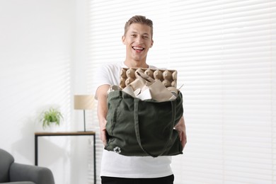 Photo of Recycling. Smiling man with bag full of different waste paper indoors