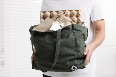 Photo of Recycling. Man with bag full of different waste paper indoors, closeup