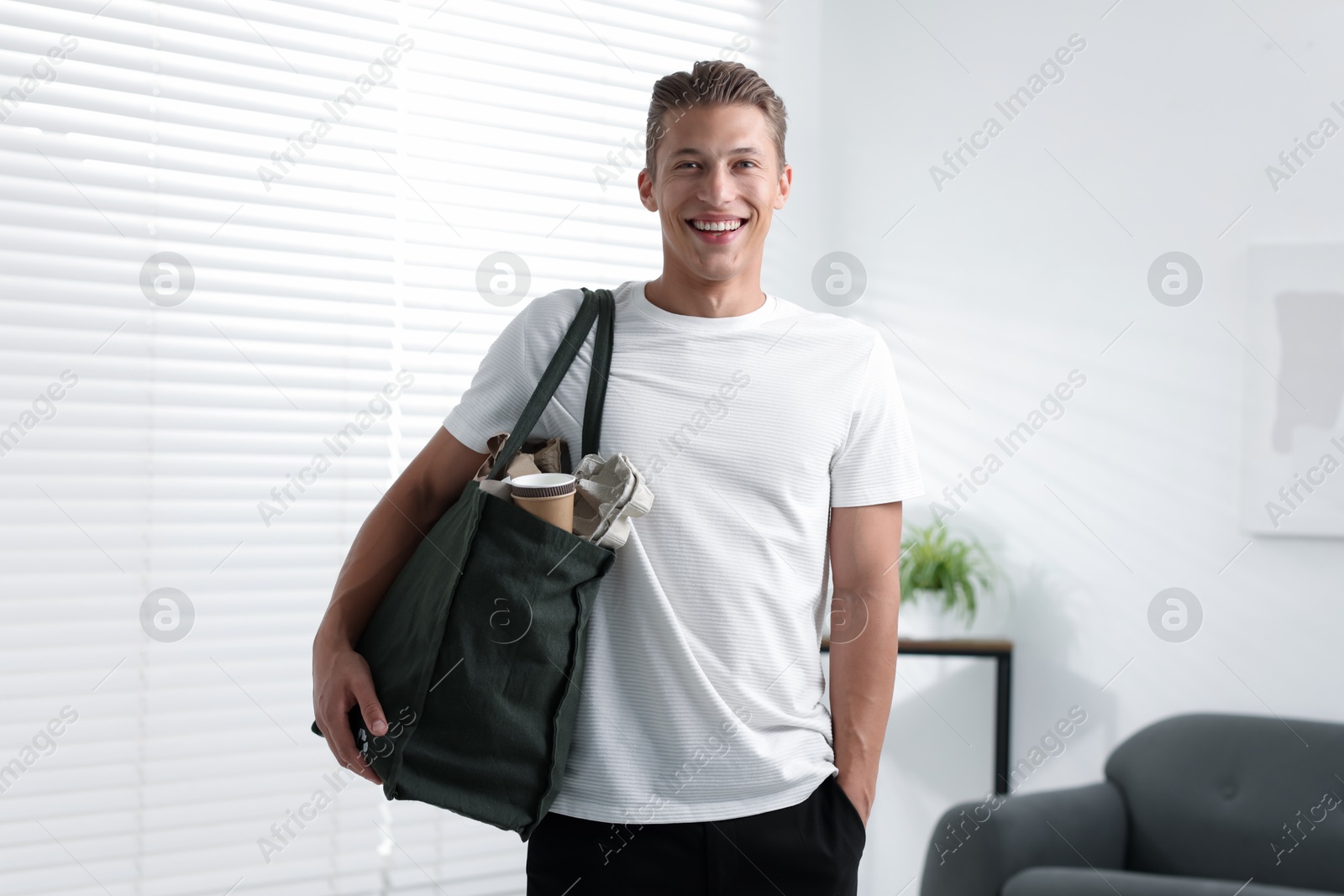Photo of Recycling. Smiling man with bag full of different waste paper indoors