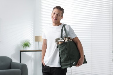 Photo of Recycling. Smiling man with bag full of different waste paper indoors