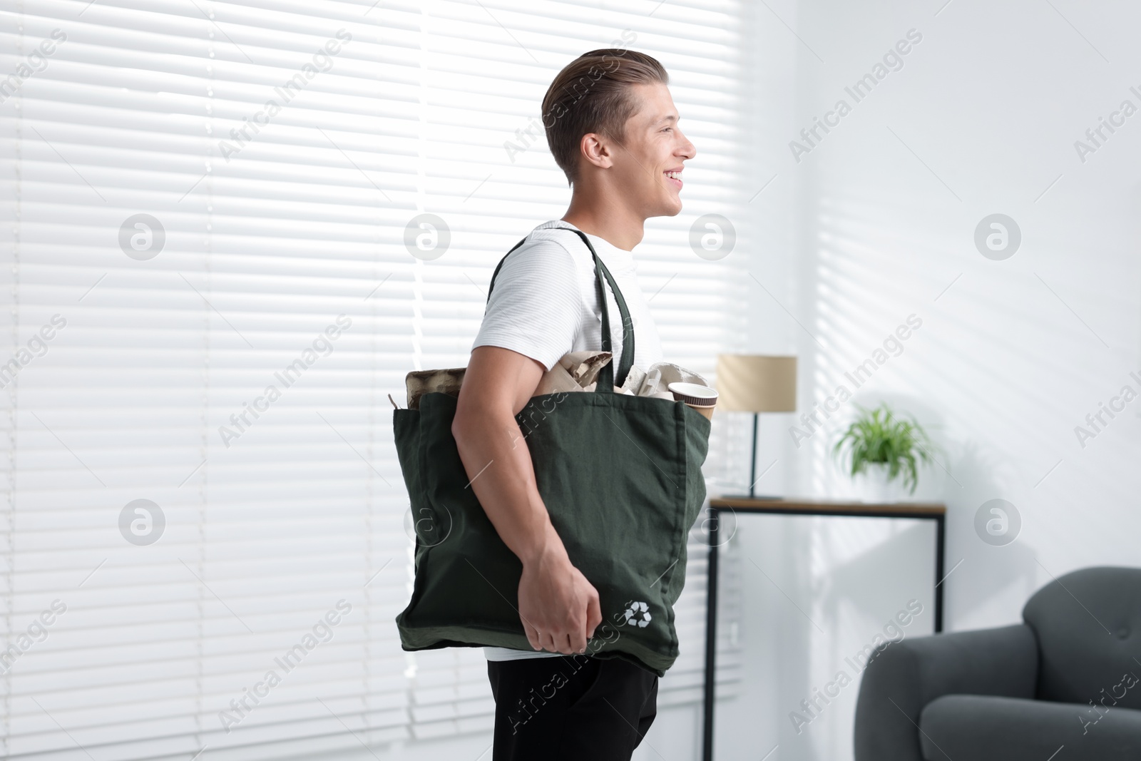 Photo of Recycling. Smiling man with bag full of different waste paper indoors