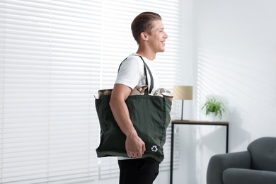 Photo of Recycling. Smiling man with bag full of different waste paper indoors
