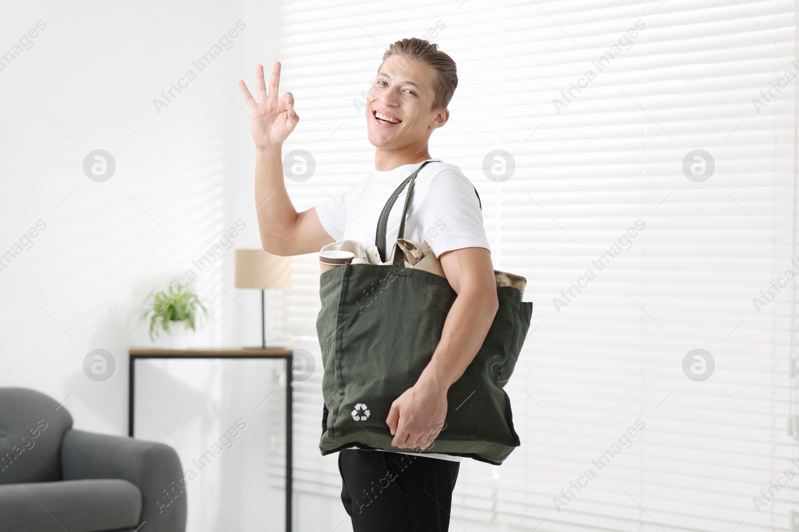 Photo of Recycling. Smiling man with bag full of different waste paper showing OK gesture indoors