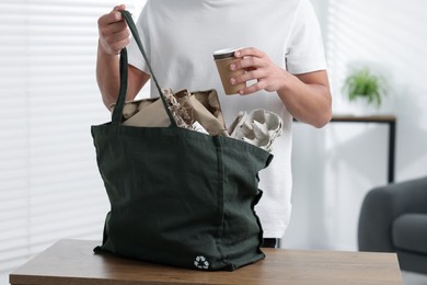Photo of Recycling. Man putting waste paper into bag at wooden table indoors, closeup