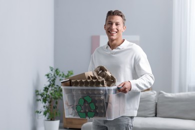 Photo of Recycling. Smiling man holding plastic box with different waste paper indoors