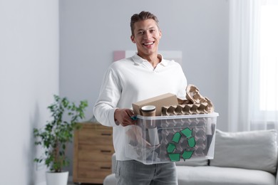 Photo of Recycling. Smiling man holding plastic box with different waste paper indoors