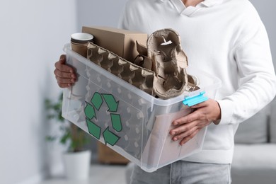 Photo of Recycling. Man holding plastic box with different waste paper indoors, closeup
