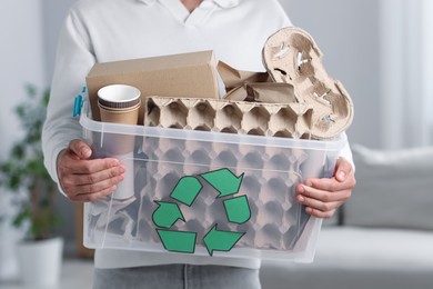 Photo of Recycling. Man holding plastic box with different waste paper indoors, closeup