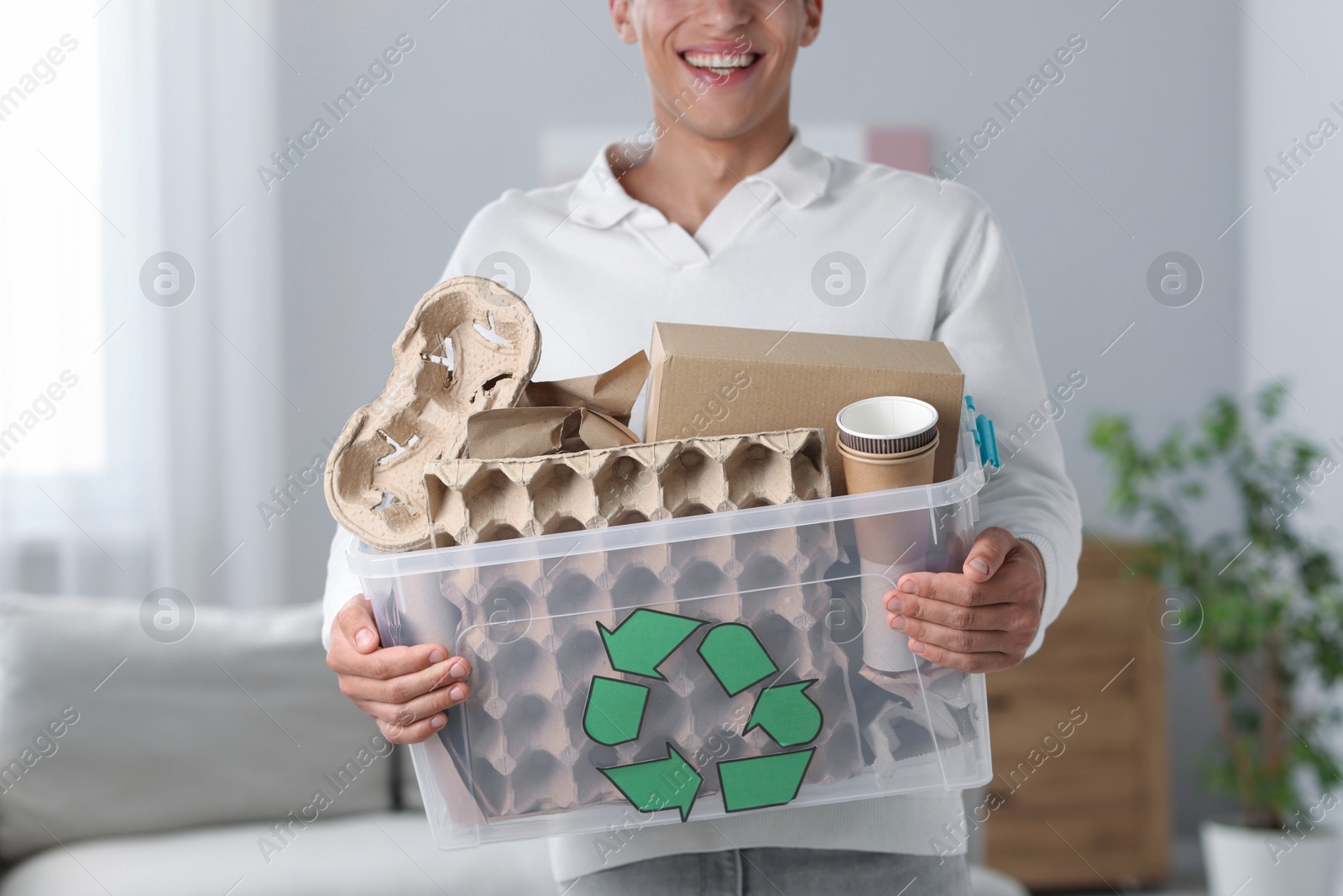Photo of Recycling. Man holding plastic box with different waste paper indoors, closeup