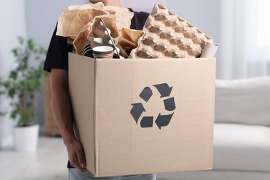 Photo of Recycling. Man holding cardboard box with different waste paper indoors, closeup