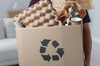 Photo of Recycling. Man holding cardboard box with different waste paper indoors, closeup