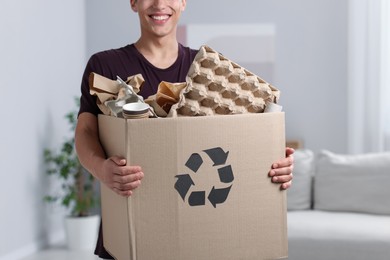 Photo of Recycling. Man holding cardboard box with different waste paper indoors, closeup
