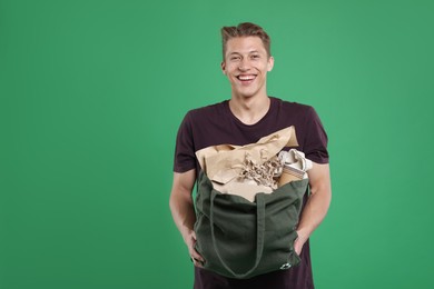 Photo of Recycling. Smiling man with bag full of different waste paper on green background