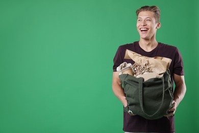 Photo of Recycling. Smiling man with bag full of different waste paper on green background. Space for text