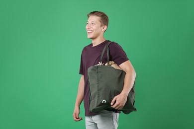Photo of Recycling. Smiling man with bag full of different waste paper on green background
