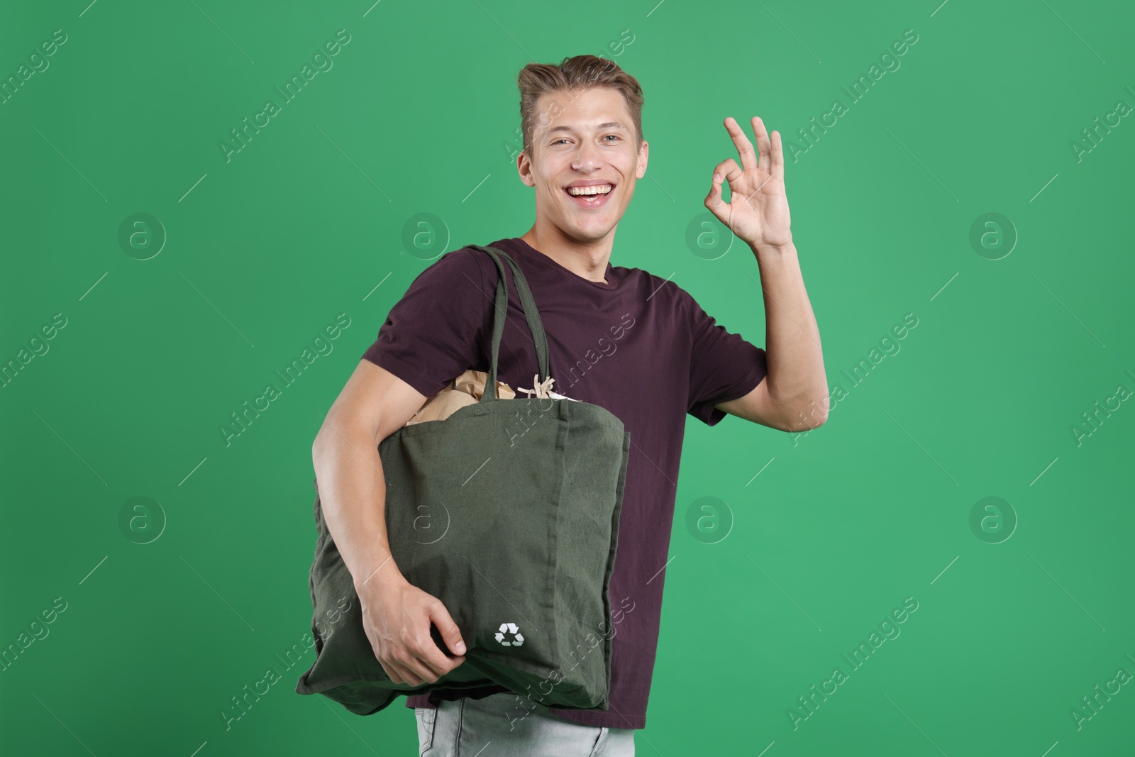 Photo of Recycling. Smiling man with bag full of different waste paper showing OK gesture on green background